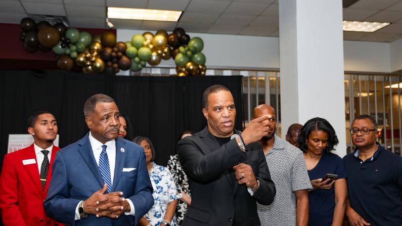 A group of people in a formal gathering, some are speaking, others are listening attentively.