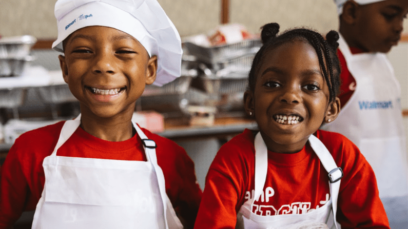 Smiling children in chef hats and aprons in a kitchen setting.