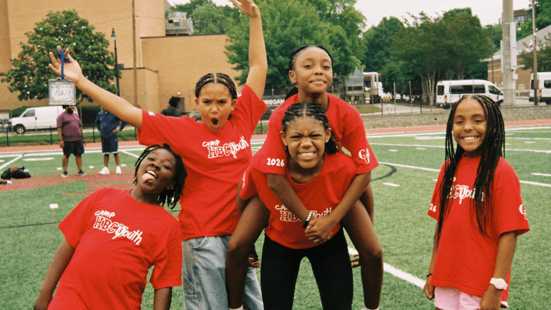 Kids in red shirts playing and smiling on a green field.