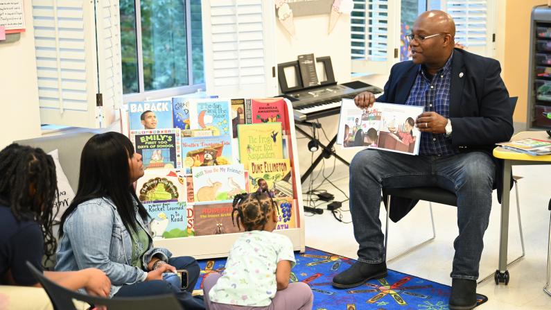 Man reading to children in a library, surrounded by colorful books.