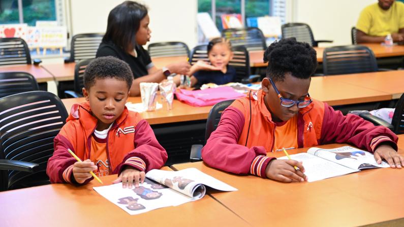 Two children in orange jackets study at a classroom table.