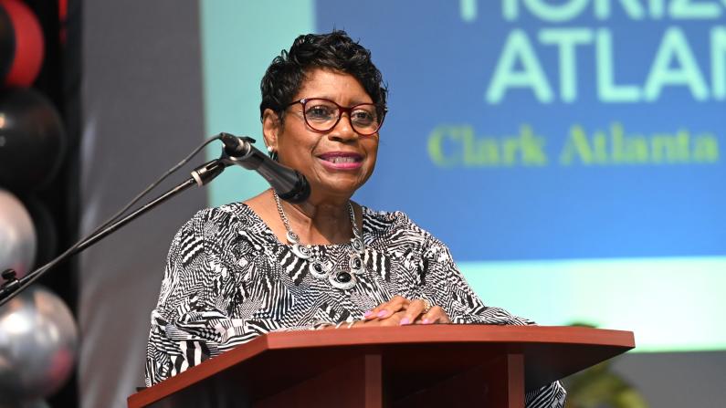 Woman speaking at a podium, smiling, indoor event.