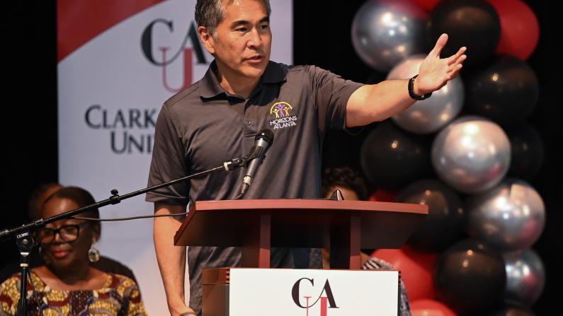 Man speaking at podium with Clark Atlanta University banner and balloons in background.
