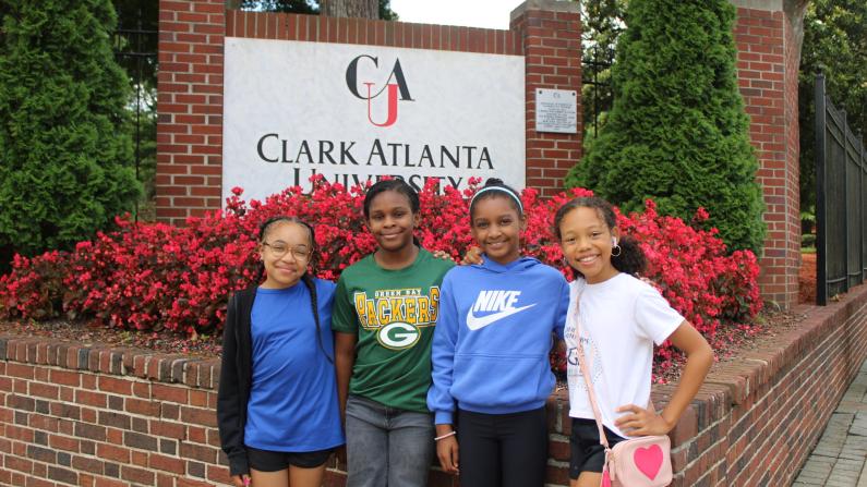 Four smiling girls stand in front of a Clark Atlanta University sign.