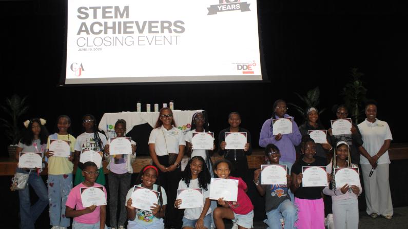 A group of people holding certificates on a stage under a "STEM Achievers" sign.