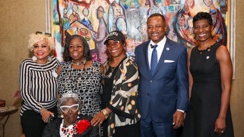 Group of people smiling in front of colorful mural, one seated.