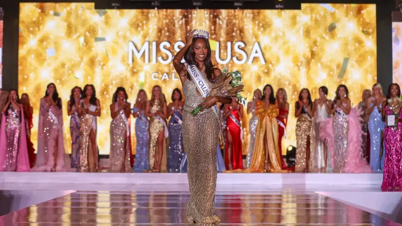 Winner in gown and crown with bouquet on stage, contestants behind her.