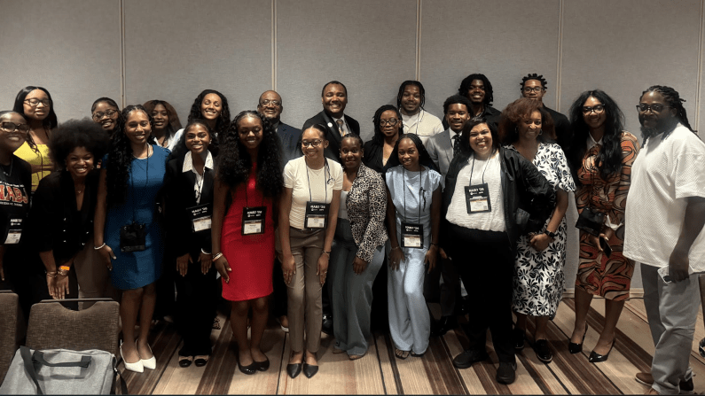 Group photo with 25 people indoors, smiling and wearing conference badges.