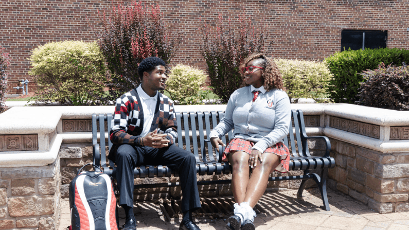 Two CAU students sitting on a bench outside, smiling and chatting.