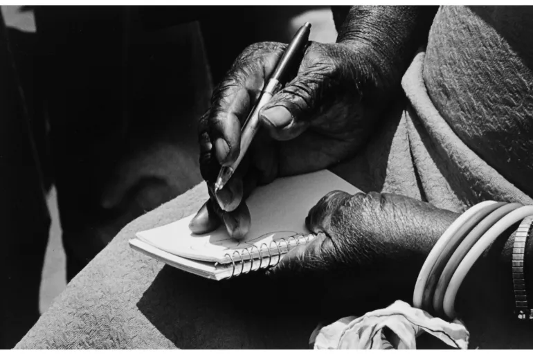 Hand writing with a pen on a notepad, wearing bangles, black and white photo.