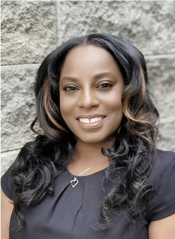 Angela Daniel International Programs Coordinator with long hair against a stone wall background.