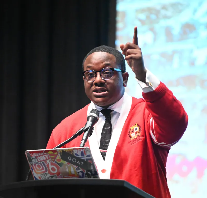 Man speaking at a podium, gesturing upward.