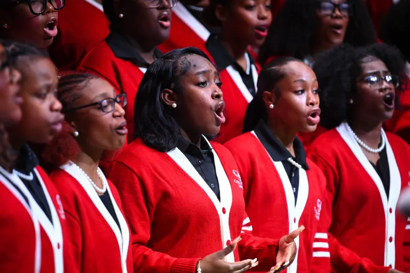 A choir sings passionately, wearing red and white cardigans.