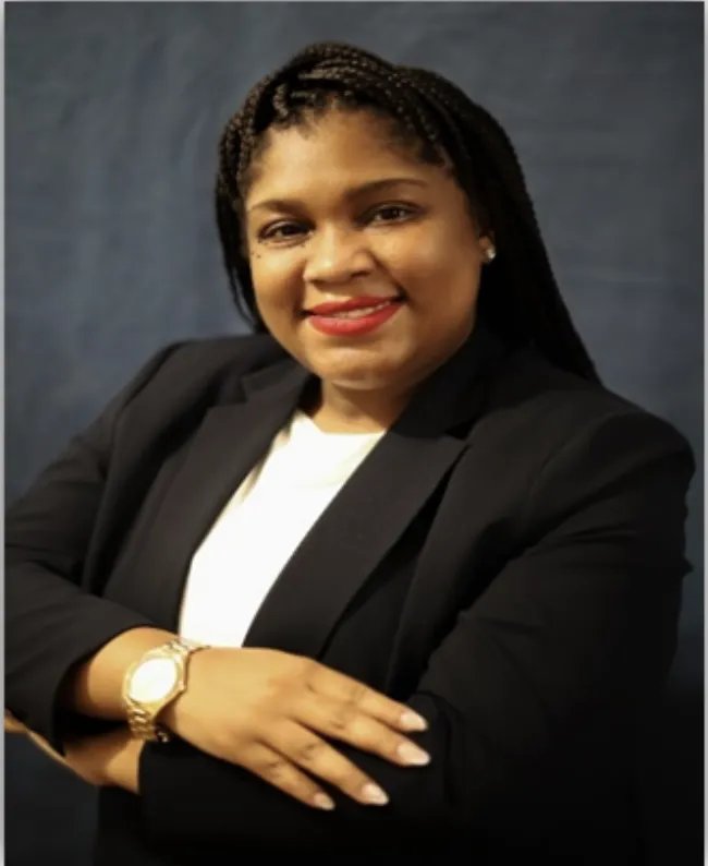 Dr. Letoyia Starr Irving in a black blazer with folded arms against blue background.