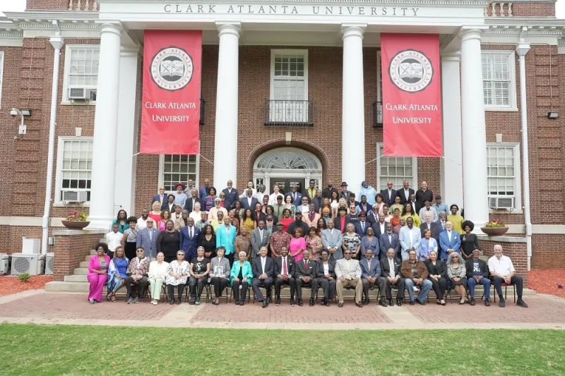 Large group gathered on steps of a red-brick building with columns and banners.