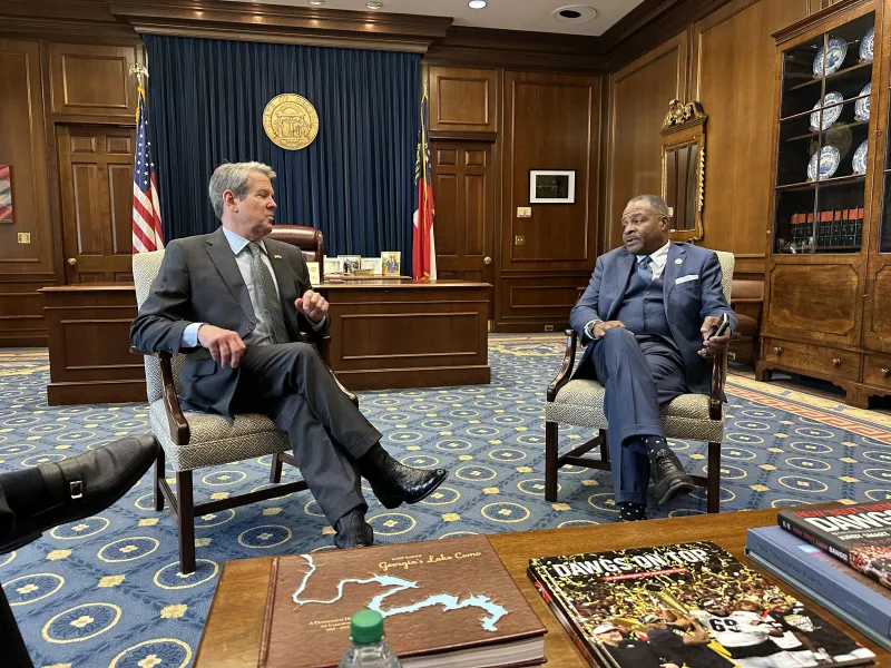 CAU President George T. French Jr. and Governor Brian Kemp seated in a formal office, engaged in conversation.