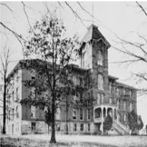 Black and white photo of a large historic brick building with a central tower.