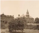 Historic sepia photo of a castle-like building with trees in the foreground.