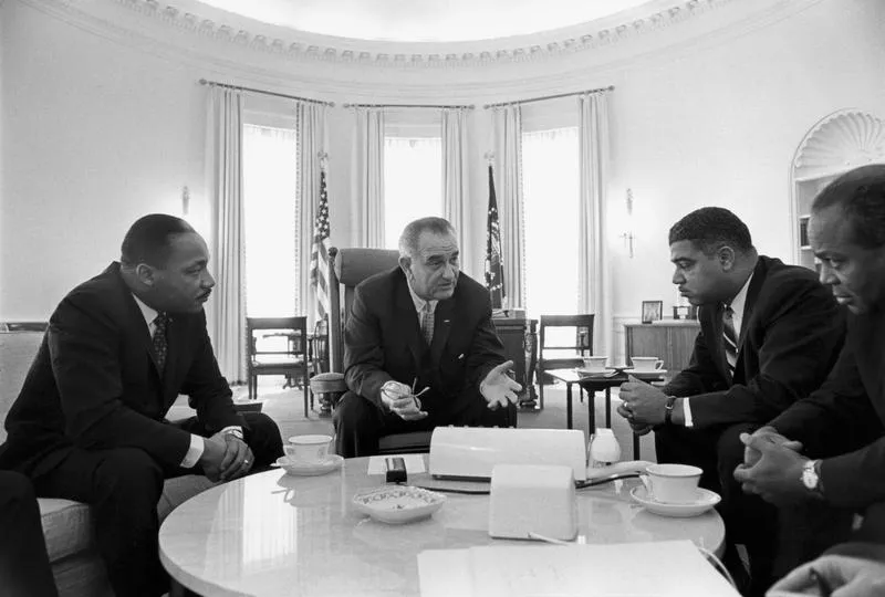 Black and white photo, four men in suits having a meeting around a table.