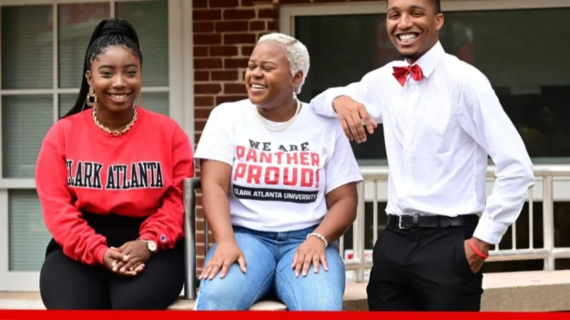 Three people smiling, wearing casual and formal college-themed attire, seated outdoors.