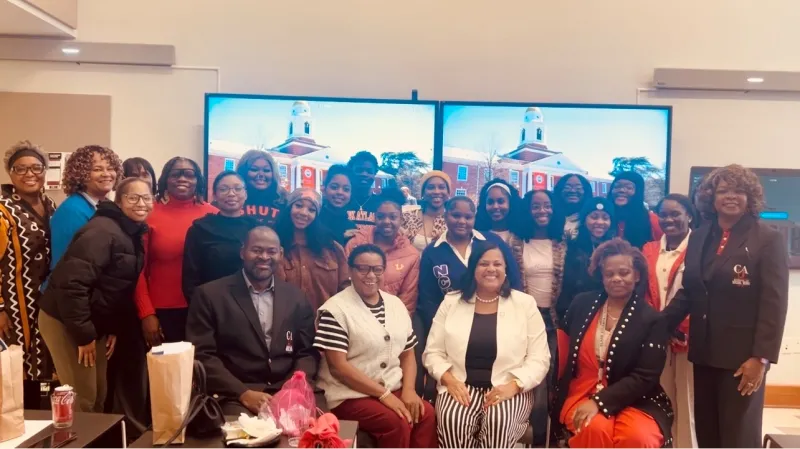 Group of BSW students smiling indoors in front of screens displaying a building.