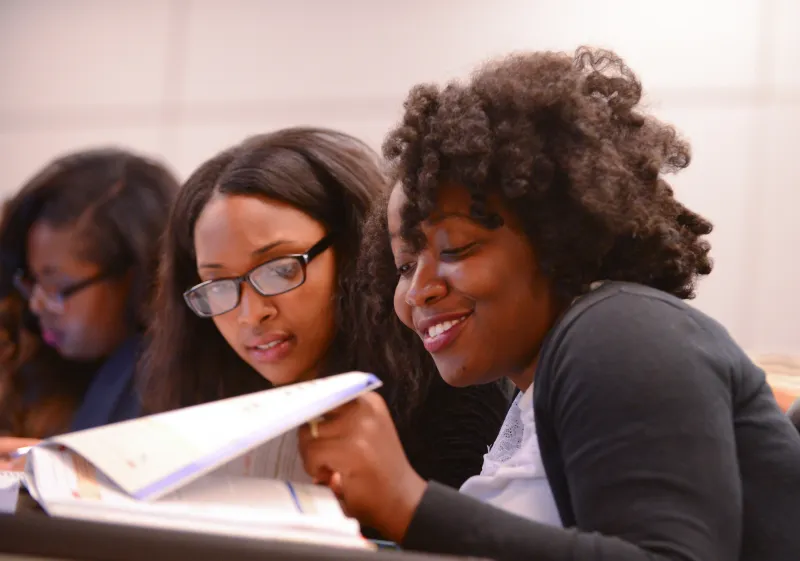 Two students reading a textbook together in a classroom setting.