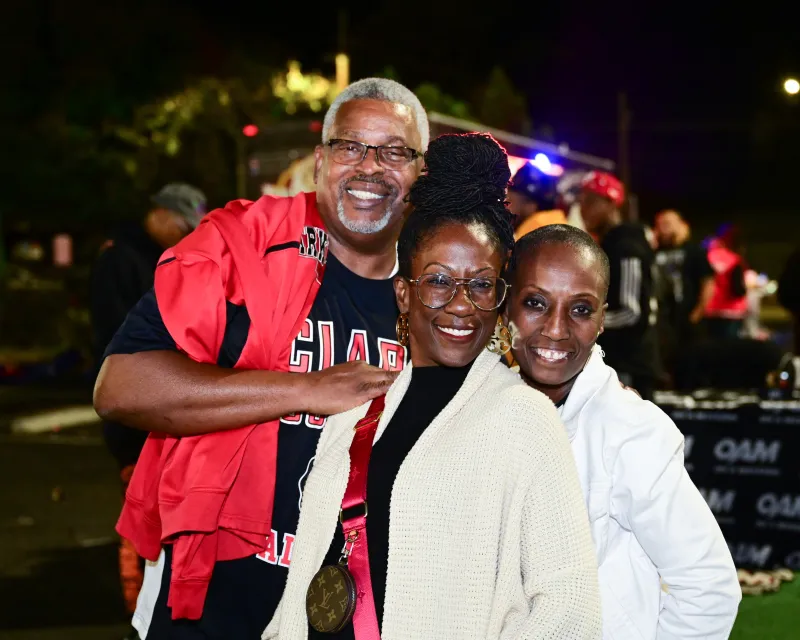 Three smiling people outdoors at night, wearing casual clothing.