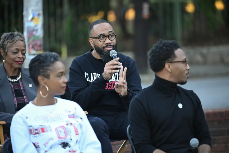 Man speaking into a microphone at an outdoor panel discussion.