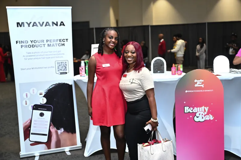 Two women smiling at an event booth with banners in the background.
