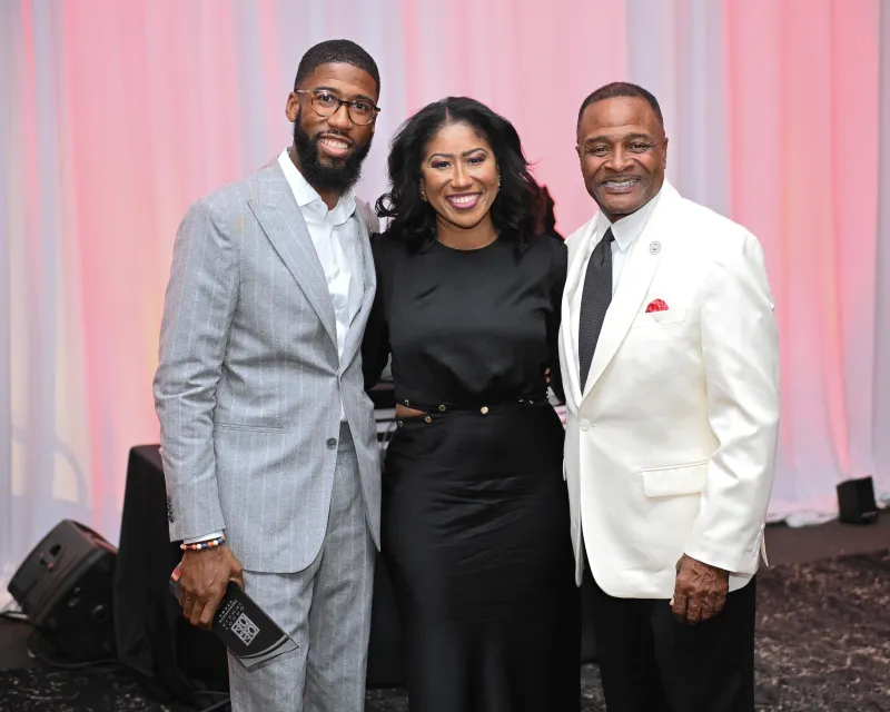Three people smiling in a formal setting, with two men and one woman.