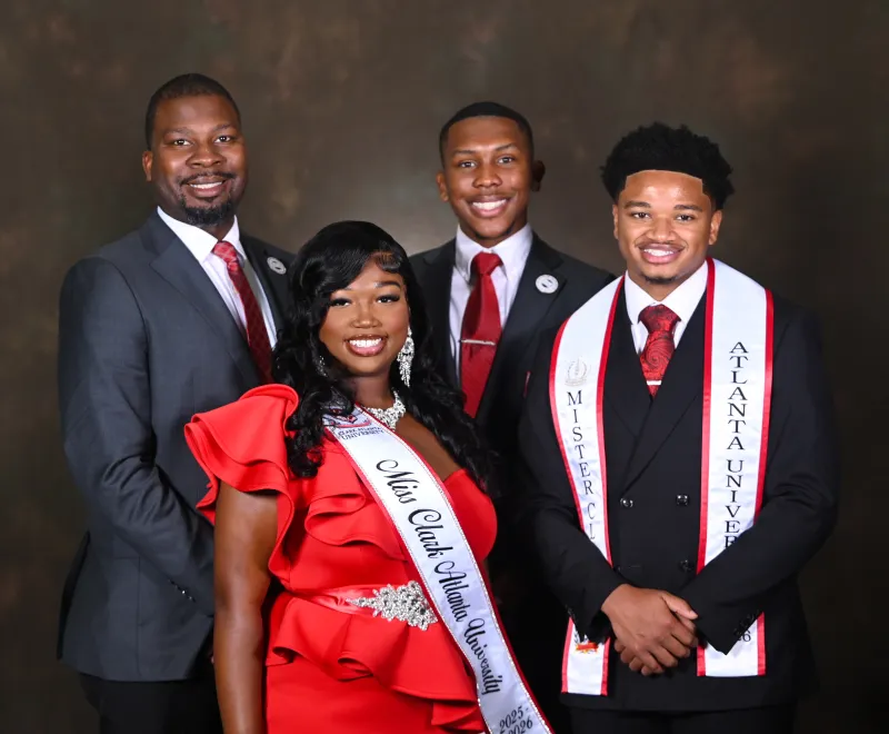 Four people in formal attire, three men in suits and one woman in a red dress with sash.