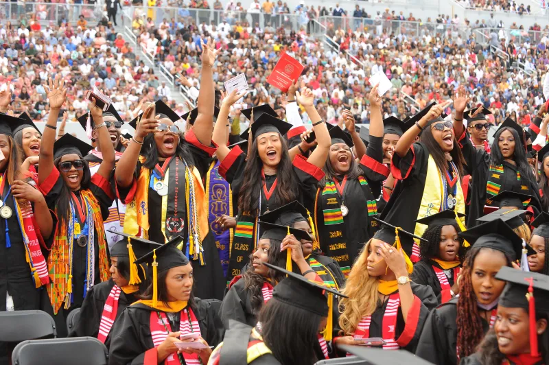 Graduates celebrating in caps and gowns at a crowded ceremony.
