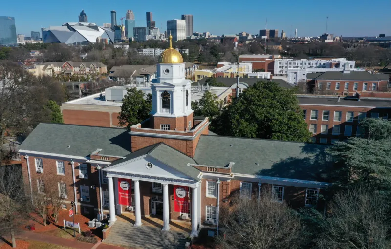 Historic brick building with a gold dome and city skyline in the background.