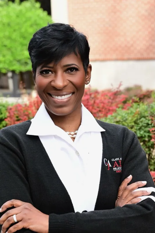 Smiling woman with short hair, in a black cardigan, standing outdoors.