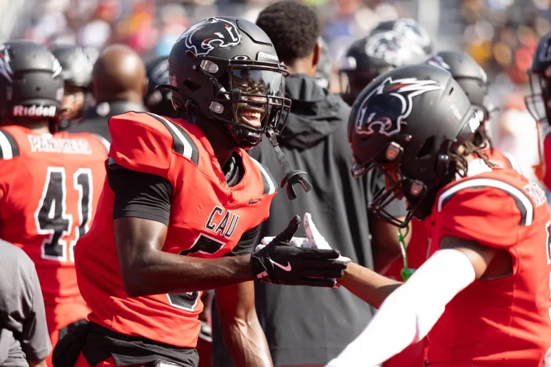 Football players in black helmets and red uniforms celebrate on the sideline.