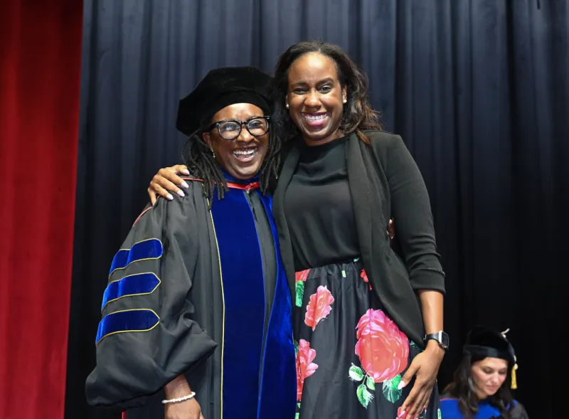 Two women smiling, one in graduation attire.