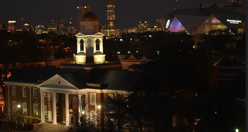 Historic building with a lit domed tower at night, city skyline in the background.