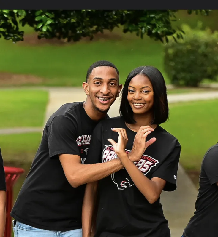 Two people smiling and posing outdoors, wearing matching black shirts.