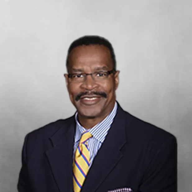 Smiling man in a suit with a yellow tie, gray background.