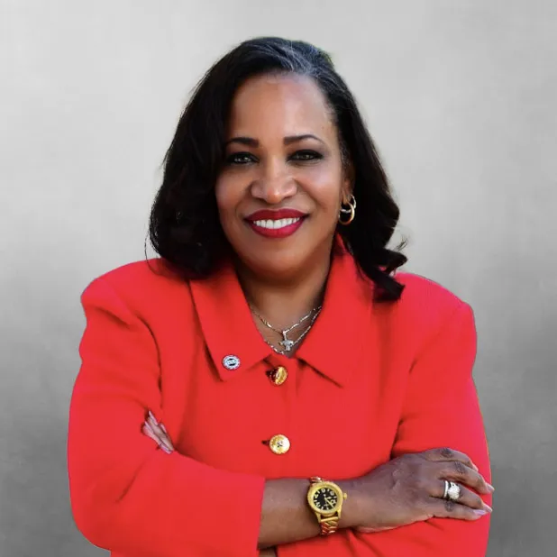 Smiling woman in red blazer with arms crossed, grey background.