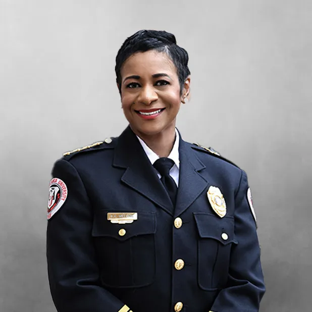 Police officer in uniform smiling, with a gray background.