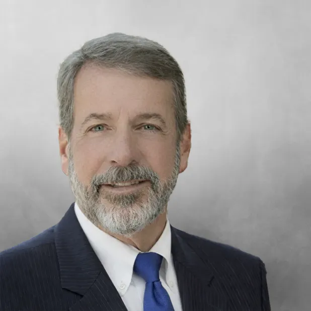 Man in suit and blue tie with gray background.