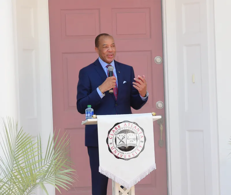 Man in a suit speaking at a podium with a red door backdrop.