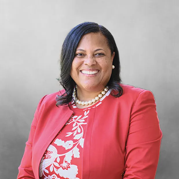 Smiling woman in a red blazer, gray background, photographed indoors.