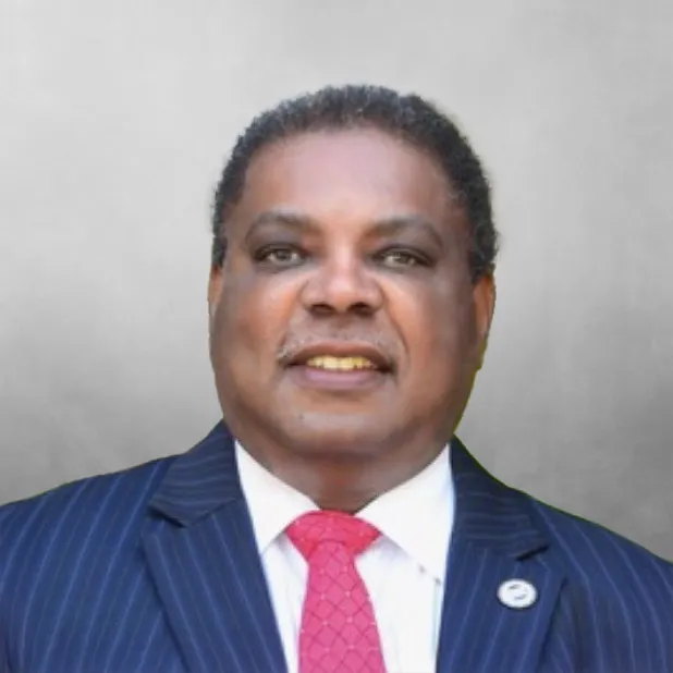 Portrait of a man in a suit with a red tie, smiling against a gray background.