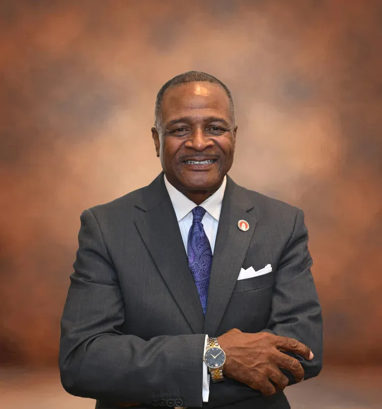 Smiling man in a suit with a brown background.