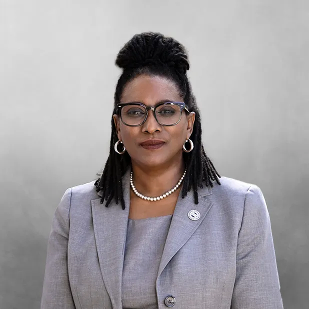 Professional woman in a gray suit with glasses, against a neutral background.