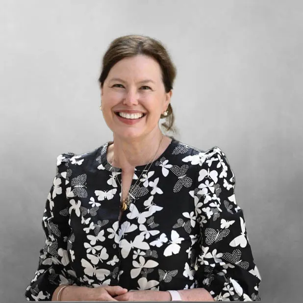 Smiling woman in butterfly-patterned blouse against gray background.