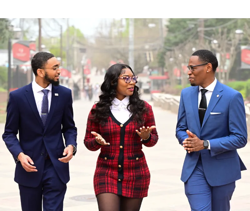Three people in formal attire walking and chatting outdoors.