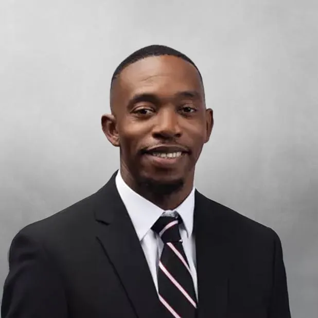 Man in a suit with a striped tie, smiling, against a gray background.